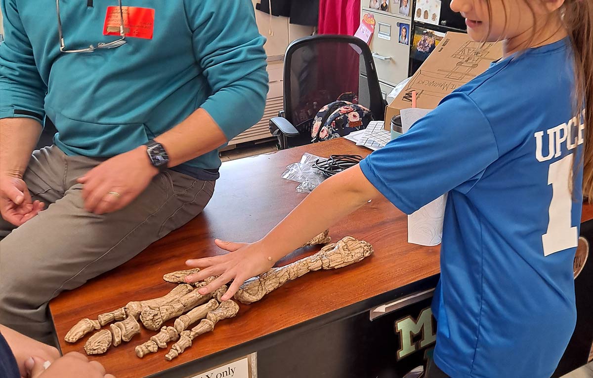 Missouri-Ozark Dinosaur Project - Dr. Peter Makovicky displays a Parrosaurus missouriensis hand and forearm (replica) to Mrs. Upchurch's student. The fossil bones were found at the Chronister Site and revealed thumb-spikes on both hands.
